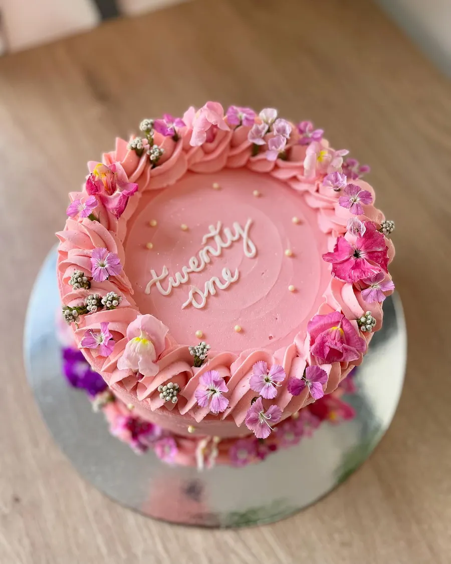 Pink cake from above with ruffles, fresh flowers and 'twenty one' in script